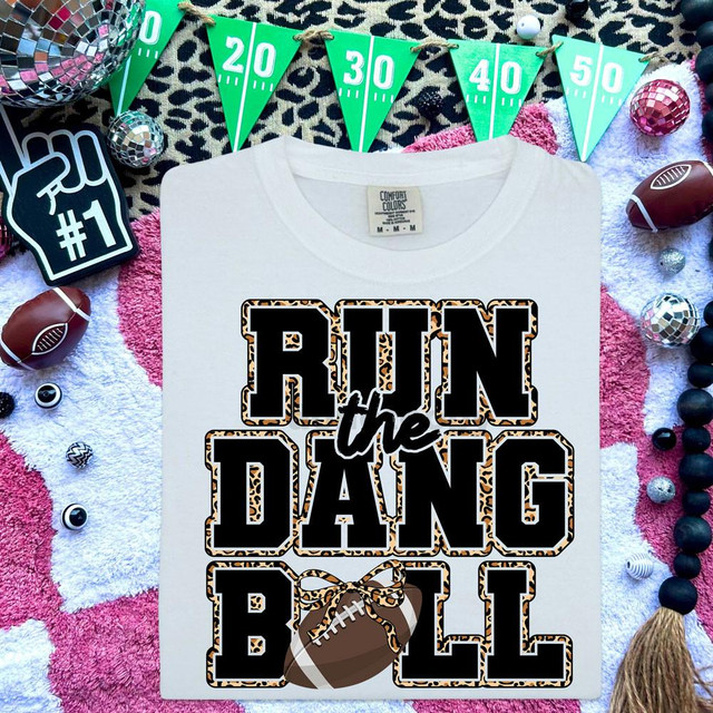 Run The Dang Ball Football DTF Heat Transfer, a white T-shirt with a football graphic and bold text for football fans surrounded by sports-themed decorations.
