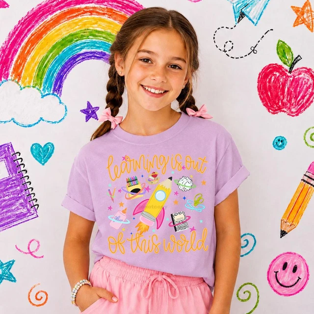 Learning Is Out Of This World DTF Heat Transfer, a colorful graphic design on a girl's purple T-shirt featuring a rocket, planets, and stars.