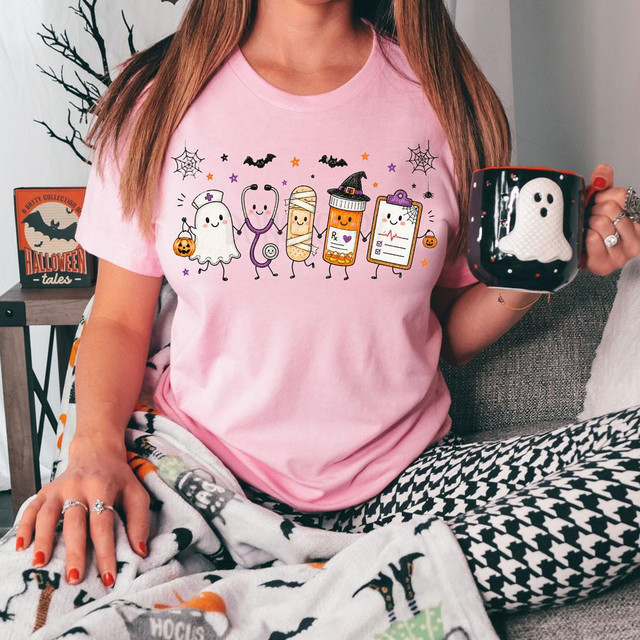Spooky Nurse DTF Heat Transfer, Halloween-themed graphic T-shirt featuring cute cartoon medical characters dressed in Halloween costumes, holding hands, with bats, spider webs, and Halloween decorations.