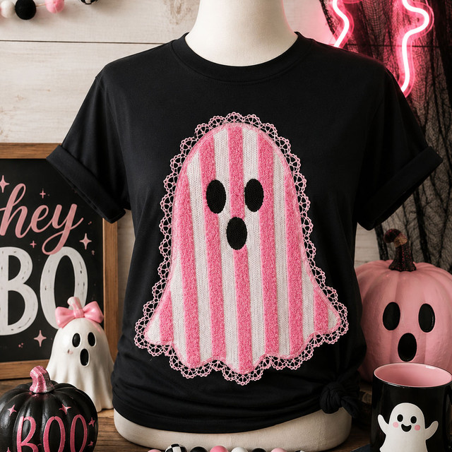 Pink and white striped ghost heat press patch with black face details and hand-sewn pink lace trim displayed on a black Halloween T-shirt.