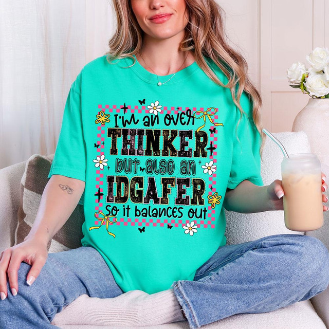 Product T-shirt, Overthinker But Also an IDGAFER DTF Heat Transfer T-shirt worn by a woman sitting on a couch holding a drink.