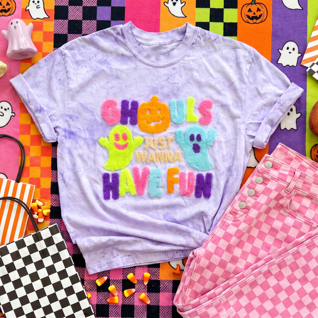 Ghouls Just Wanna Have Fun Fluffy Halloween Apparel Patch, colorful fuzzy Halloween-themed patches on a purple tie-dye shirt with pumpkin, ghost, and playful text surrounded by Halloween decorations.