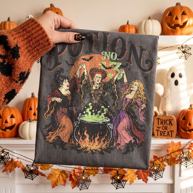 Potion No. 13 Witches DTF Transfer, vintage Halloween cauldron design on fabric with three witches around a bubbling cauldron, Halloween decorations in background.