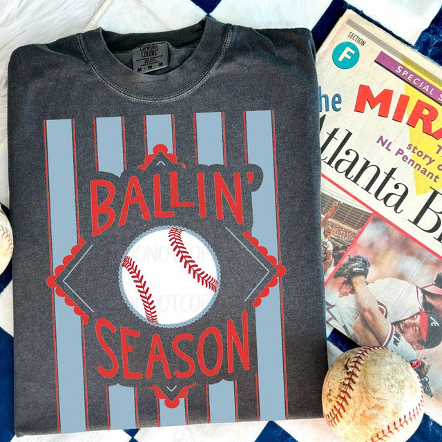 Ballin’ Season Baseball DTF Transfer, a baseball-themed custom transfer design on a dark gray T-shirt with a baseball graphic and bold red and blue text.