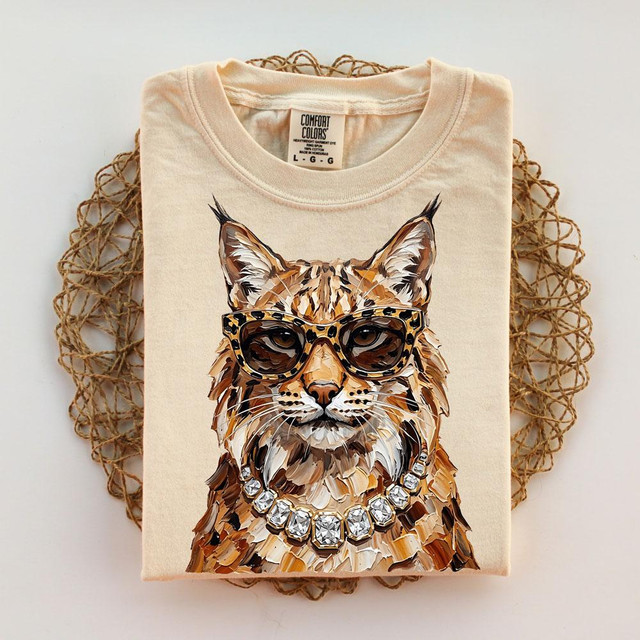 Glam Bobcat DTF Transfer | Leopard Glasses Bobcat DTF, a graphic T-shirt featuring a bobcat wearing leopard-print glasses and a jeweled necklace.