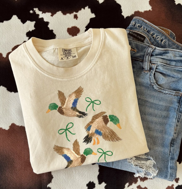 Hand-painted style mallard duck DTF transfer with three flying ducks and green coquette bows on a cream shirt