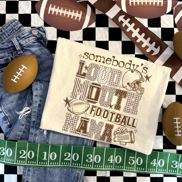 Somebody's Loud Mouth Football Mama DTF Transfer, game day football-themed design on a fabric piece, with footballs, denim shorts, and a green measuring tape on a checkered background.