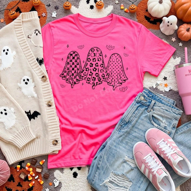 Trio of Patterned Ghosts DTF Transfer, cute Halloween design on a pink T-shirt with black and white ghost and bat patterns, surrounded by Halloween-themed items like pumpkins, ghosts, candy, and sneakers.