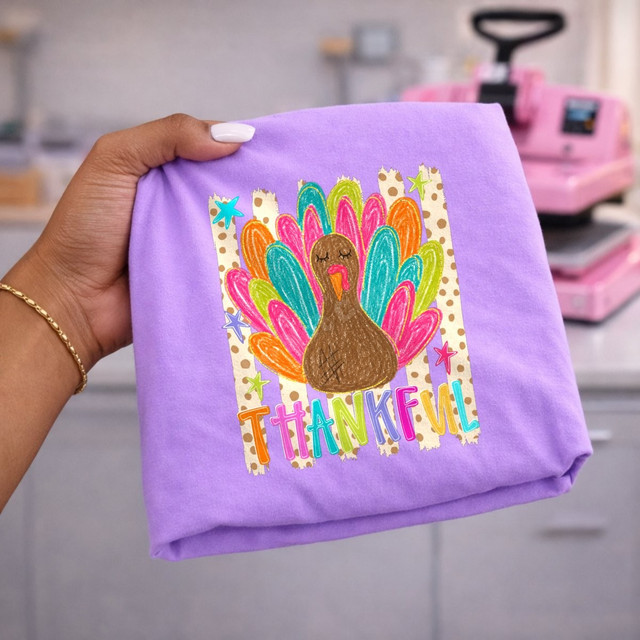 Thankful DTF transfer with colorful hand-drawn turkey, rainbow feathers, and polka dot striped background on a purple shirt