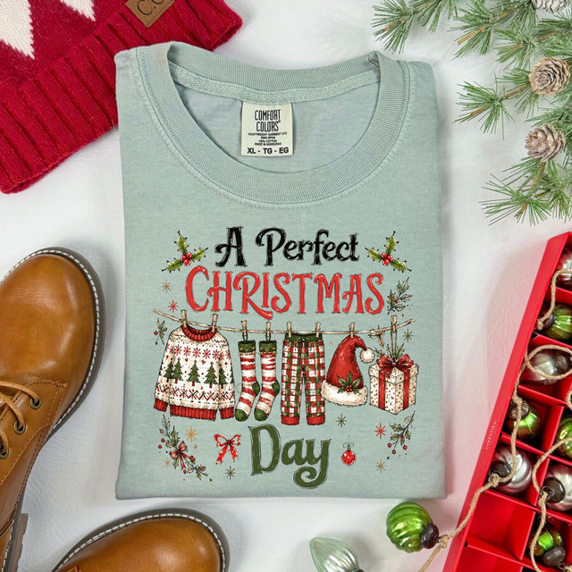A Perfect Christmas Day DTF transfer with illustrated holiday clothesline featuring a sweater, stockings, plaid pajama pants, Santa hat, and gift box