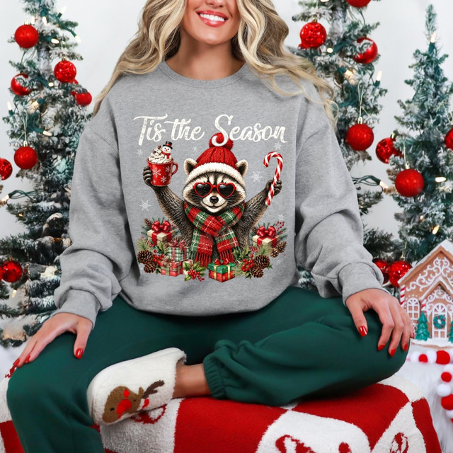 Tis the Season DTF transfer featuring a raccoon in a santa hat and heart sunglasses holding hot cocoa and a candy cane, surrounded by presents and holly