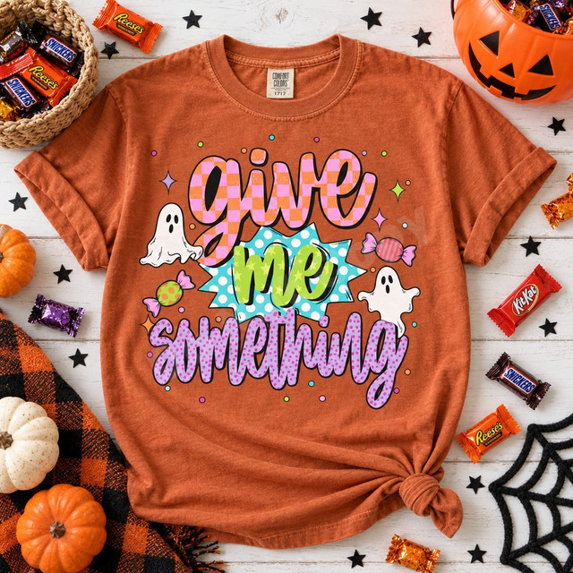 Give Me Something Halloween DTF transfer with checkered and polka-dot bubble lettering, cartoon ghosts, and striped candy illustrations Shown on a Burnt Orange t-shirt.