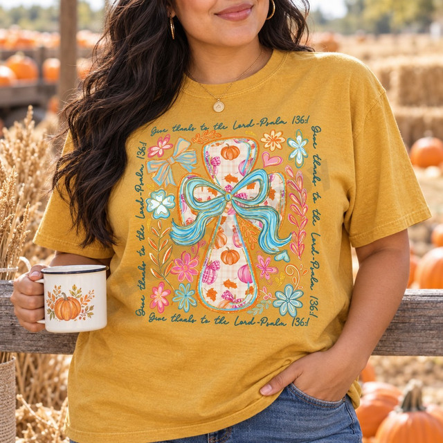 Give Thanks to the Lord Psalm 136:1 fall DTF transfer with pumpkin plaid cross, teal ribbon bow, and pink, orange, and blue florals Shown on a Mustard t-shirt.