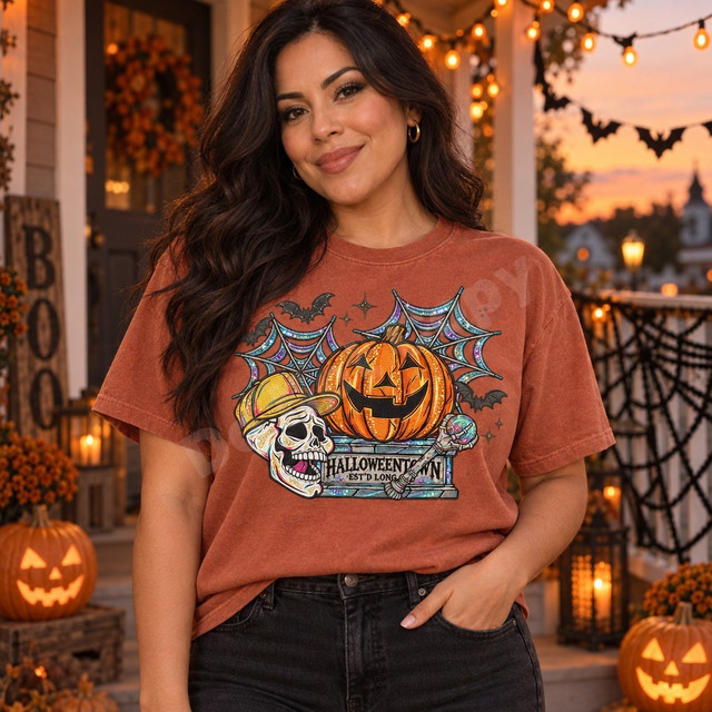 Halloweentown DTF transfer with glittery jack-o-lantern, stone marker, spider webs, bats, and a grinning skull in a yellow trucker hat holding a glowing staff Shown on a Terracotta t-shirt.