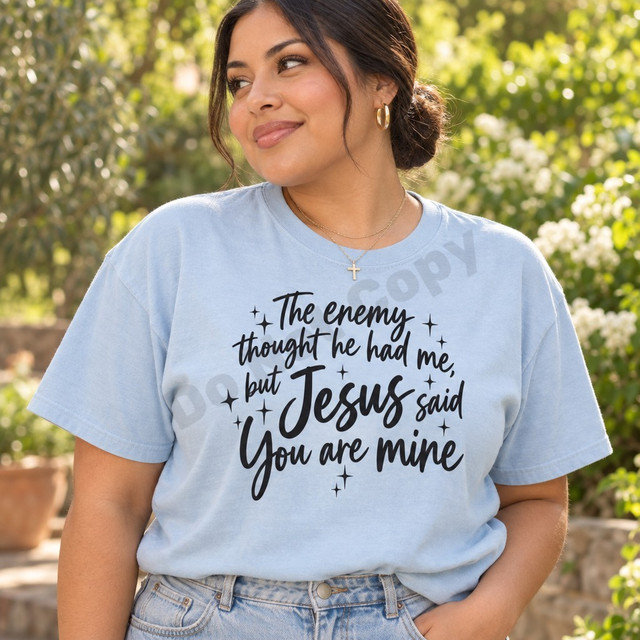 The Enemy Thought He Had Me But Jesus Said You Are Mine faith DTF transfer in black brush-script lettering with hand-drawn sparkle stars Shown on a Ice Blue t-shirt.