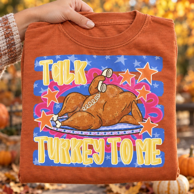 Talk Turkey To Me Thanksgiving DTF transfer with cartoon roasted turkey chatting on a retro telephone, surrounded by orange stars on a blue starred background Shown on a Yam t-shirt.