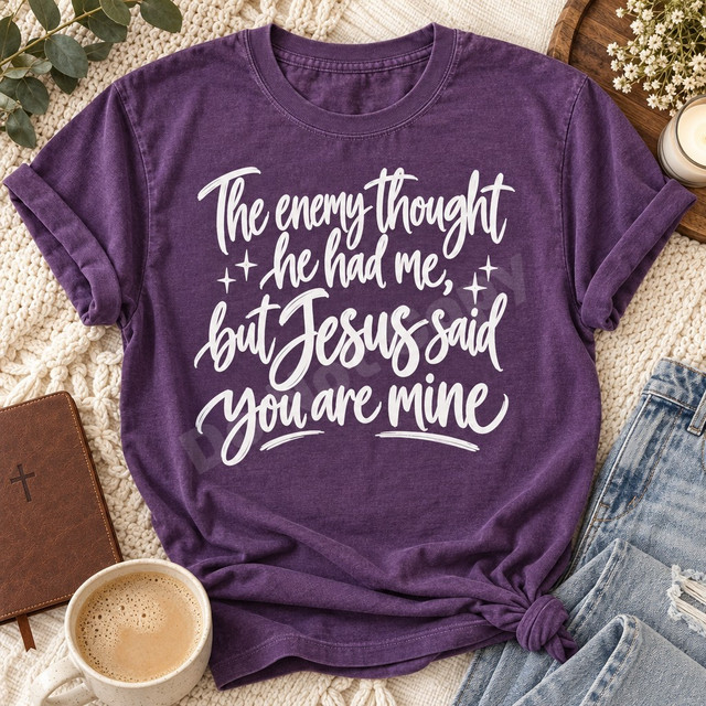 The enemy thought he had me, but Jesus said you are mine DTF transfer in bold white hand-brushed script with sparkle star accents Shown on a Grape t-shirt.