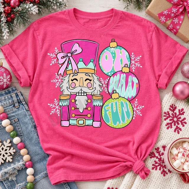 Oh What Fun Nutcracker DTF Transfer | Pink & Mint Christmas Design, festive pink shirt featuring a colorful nutcracker, pastel ornaments spelling “Oh What Fun,” and snowflakes, styled with Christmas decorations.