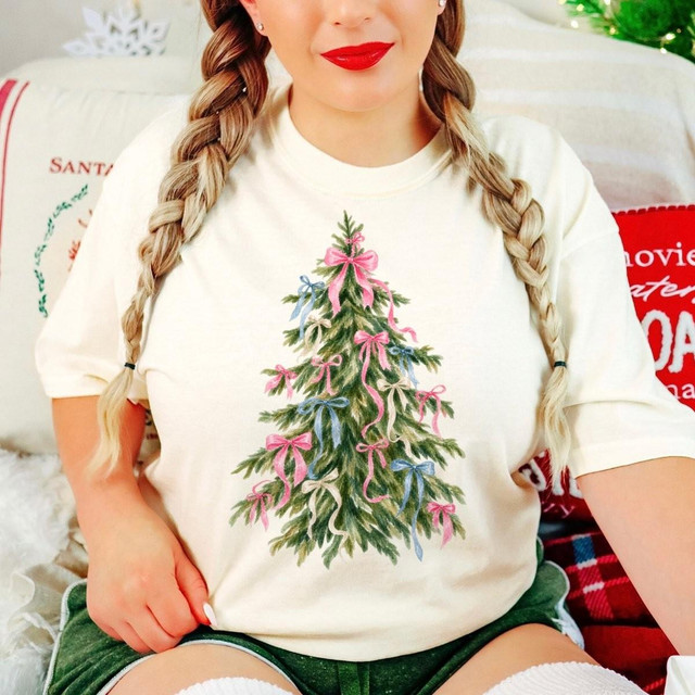 Bow Christmas Tree DTF Transfer | Watercolor Holiday Design, watercolor evergreen Christmas tree decorated with pink and blue bows printed on a cream T-shirt worn by a woman