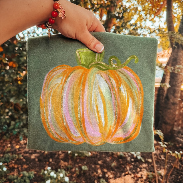 Watercolor-style pumpkin DTF transfer in orange, pink, and gold with a green curled vine on a sage green shirt