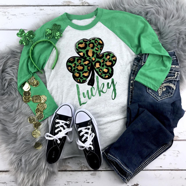 Lucky Leopard Shamrock Screen Print Transfer, a green and black leopard print shamrock with the word Lucky underneath, surrounded by green accessories and casual clothing.
