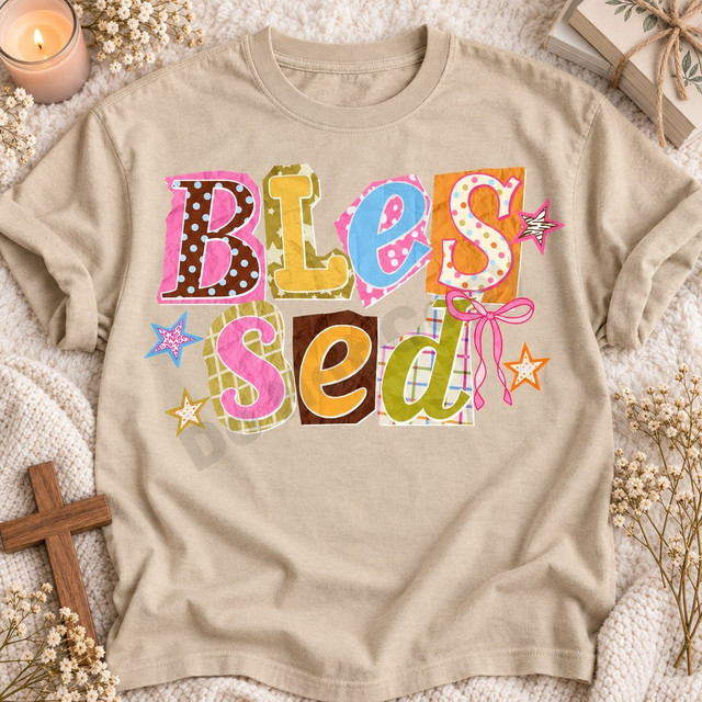 Blessed DTF transfer with scrapbook-style polka-dot, plaid, and star paper cutout letters and a pink ribbon bow Shown on a Sandstone t-shirt.