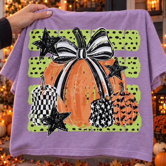 Fall pumpkin DTF transfer with a large orange pumpkin topped by a black-and-white striped bow, surrounded by checkerboard, star-print, and bat-print pumpkins and black stars on a green polka-dot background Shown on a Orchid t-shirt.