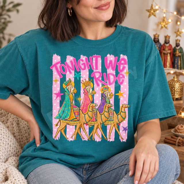 Tonight We Ride DTF transfer featuring the Three Wise Men riding camels in colorful robes, on a pink and white polka-dot striped background with scattered stars Shown on a Lagoon t-shirt.
