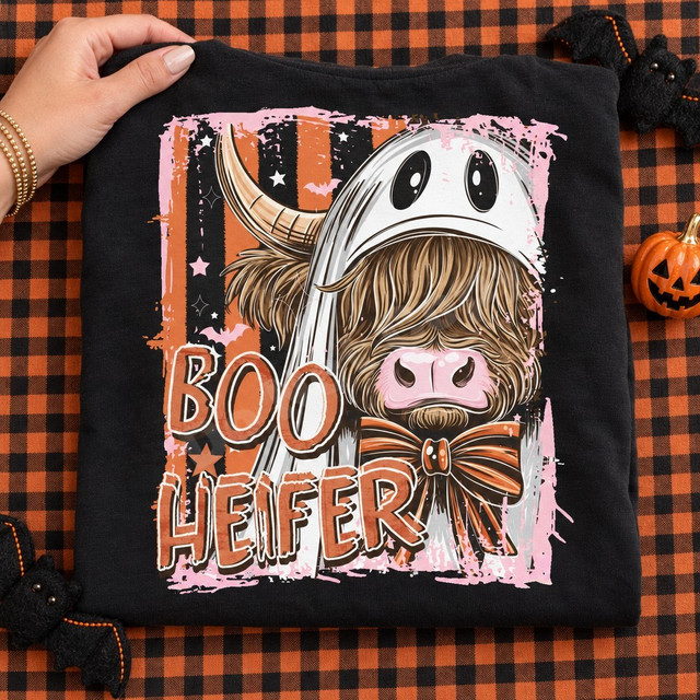 Boo Heifer Halloween DTF transfer featuring a highland cow in a ghost costume with a bow, set against an orange and black striped backdrop with bats and stars Shown on a Black t-shirt.