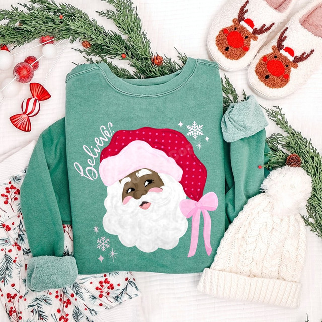 Believe Santa DTF transfer with polka dot hat, pink bow, and snowflake accents on a green sweatshirt