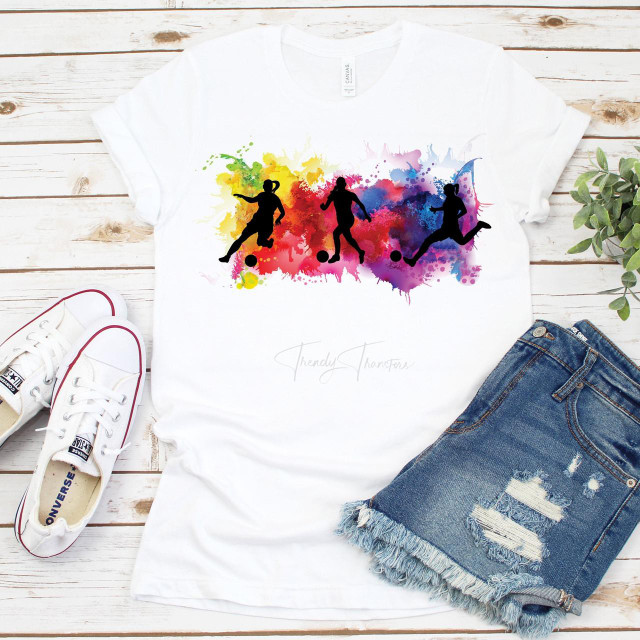 Watercolor Soccer Silhouette Sublimation Transfer, colorful silhouette design of three soccer players against a vibrant watercolor splash background on a white t-shirt.