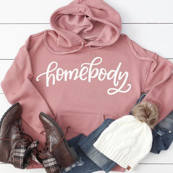 Homebody ADULT Screen Print Transfer, pink hoodie with 'homebody' text design, paired with boots, jeans, and a white knit hat with pom-pom.