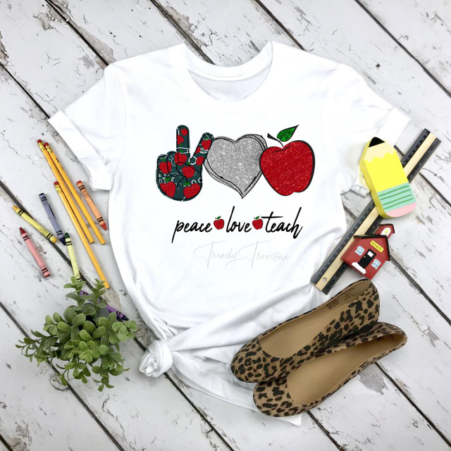 Peace love teach heart apple glitter sublimation transfer, colorful design featuring a peace sign, heart, and apple on a white T-shirt with surrounding stationery and accessories.