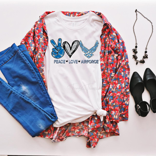 Peace Love Airforce glitter heart sublimation transfer, displayed on a white t-shirt with peace sign, heart and eagle symbols, surrounded by blue pants, black shoes, necklace, and colorful floral shirt.
