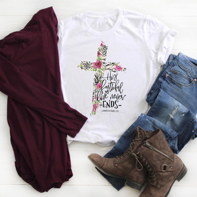 His Faithful Love Never Ends Leopard Zebra Rose Patterned Cross Sublimation Transfer, white T-shirt with a cross design featuring leopard, zebra, and rose patterns, laid out with denim jeans, brown boots, and a maroon cardigan on a white wooden surface.