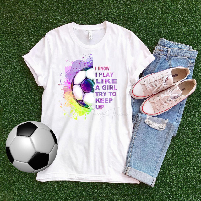 I Know I Play Like a Girl Try To Keep Up Soccer Sublimation Transfer T-shirt, front view with colorful soccer ball graphic on white T-shirt laid on artificial grass with denim jeans and sneakers nearby