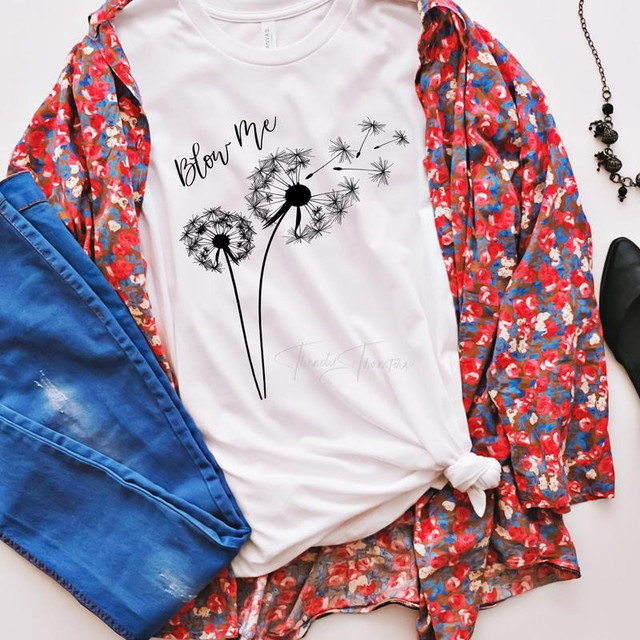 Blow Me Dandelion Sublimation Transfer, image of a white T-shirt with a dandelion design and text, surrounded by blue jeans, a floral jacket, black shoes, and accessories.