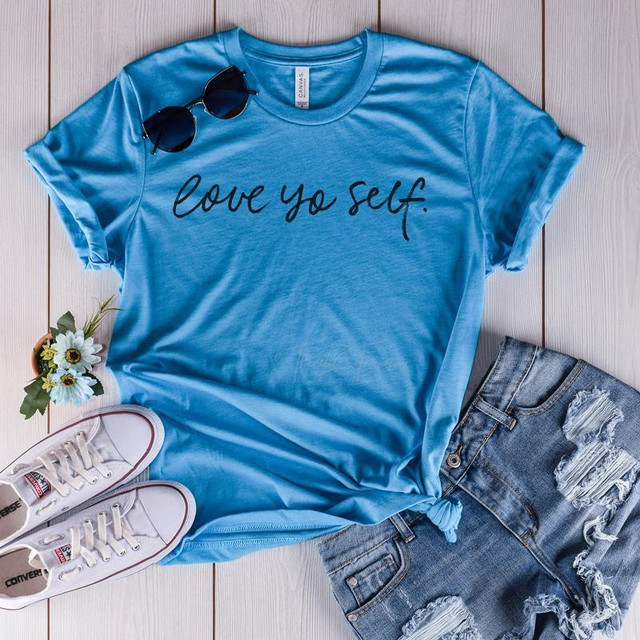 Love Yo Self Screen Print Transfer, blue T-shirt with black script lettering and casual denim shorts, with accessories like white sneakers, sunglasses, and a small bouquet of flowers.
