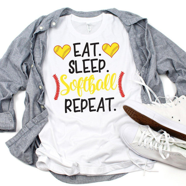 Eat Sleep Softball Sublimation Transfer, a white T-shirt with a design featuring yellow hearts with baseball stitching, game-related text, and red fern accents, laid flat with a gray shirt and white sneakers.