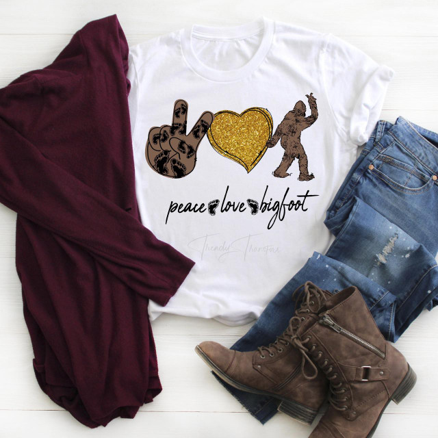 Peace Love Bigfoot glitter heart Sublimation Transfer, t-shirt featuring a glittery gold heart with a Bigfoot silhouette and peace signs, surrounded by casual clothing and footwear.