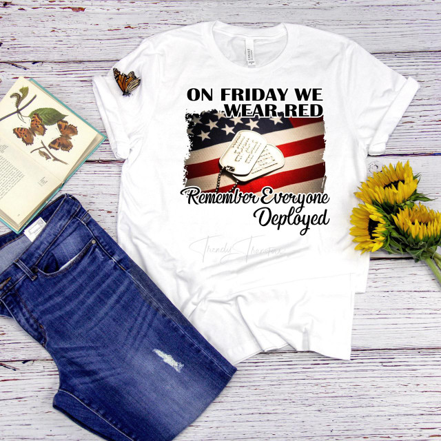 On Friday we wear red dog tags flag Remember Everyone Deployed sublimation transfer T-shirt, featuring American flag and military dog tags design, laid on a wooden surface with jeans, sunflower bouquet, and a book with butterflies