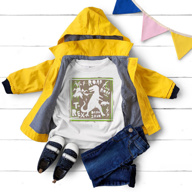 Dino collage sublimation transfer, colorful dinosaur themed design on a white T-shirt laid out with kids' clothing and accessories on white wooden surface.
