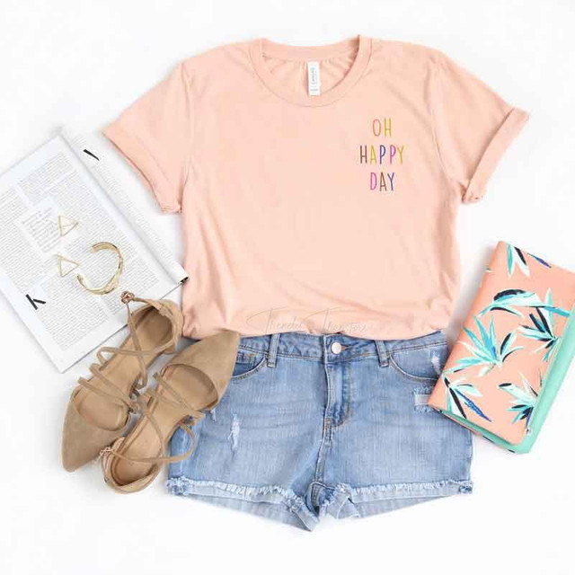 Oh Happy Day Pocket Screen Print Heat Transfer, pink t-shirt with colorful 'Oh Happy Day' print, paired with denim shorts, beige shoes, and accessories on a white background.