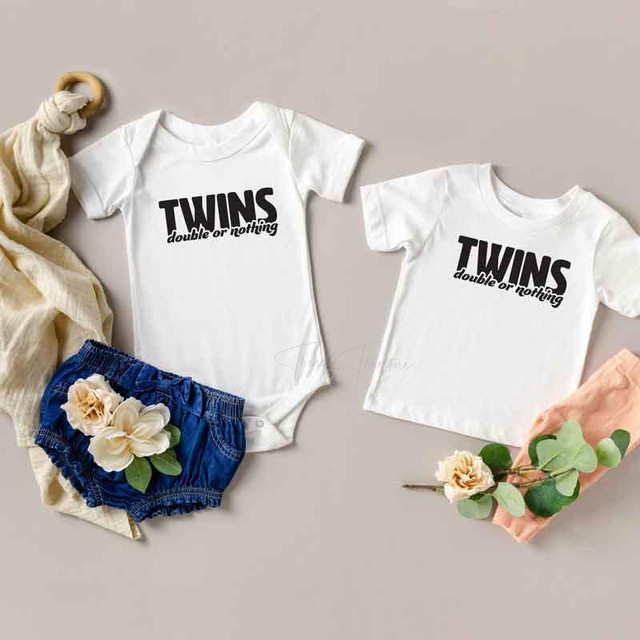 Twins Double Or Nothing Sublimation Transfer, white baby bodysuits with black text, one with long sleeve and one with short sleeve, displayed with blue shorts, flowers, and fabric accessories.