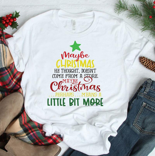Maybe Christmas Means A Little Bit More Sublimation Transfer, white T-shirt with Christmas-themed quote and green star graphic, festive holiday decorations surrounding it.