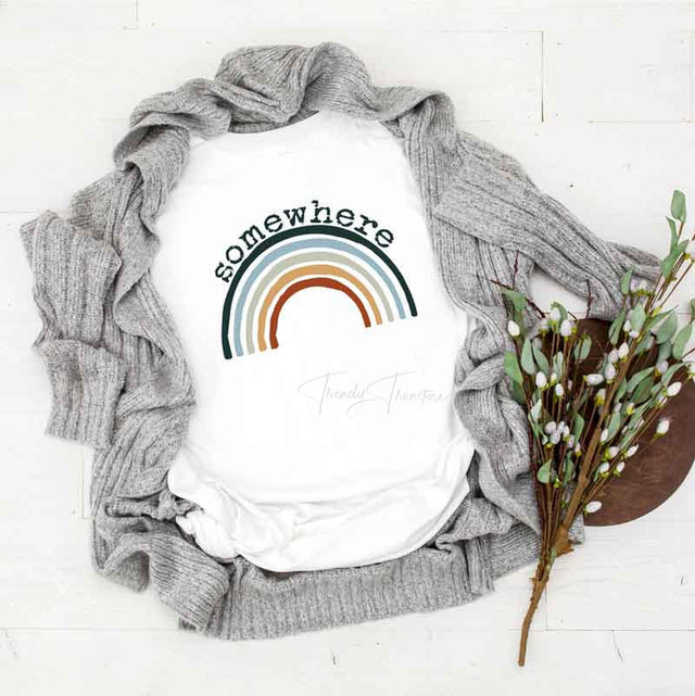 Somewhere Over the Rainbow Sublimation Transfer, white t-shirt with rainbow design and the word 'somewhere' printed on it, surrounded by a gray knit sweater and a bouquet of white flowers with green leaves.