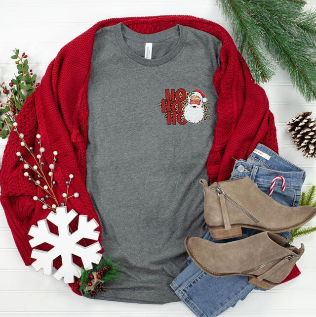 HO HO HO Santa HAT/POCKET Screen Print Transfer, Christmas themed gray T-shirt with Santa face graphic and red lettering, surrounded by holiday decorations, jeans, and taupe ankle boots.