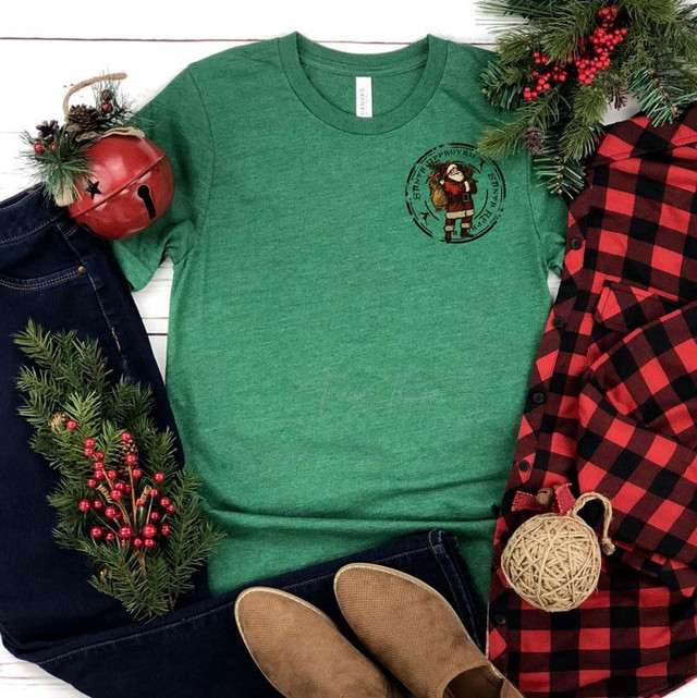 Santa Approved HAT/POCKET Screen Print Heat Transfer, green T-shirt with Santa graphic print, surrounded by Christmas decorations and plaid shirt.