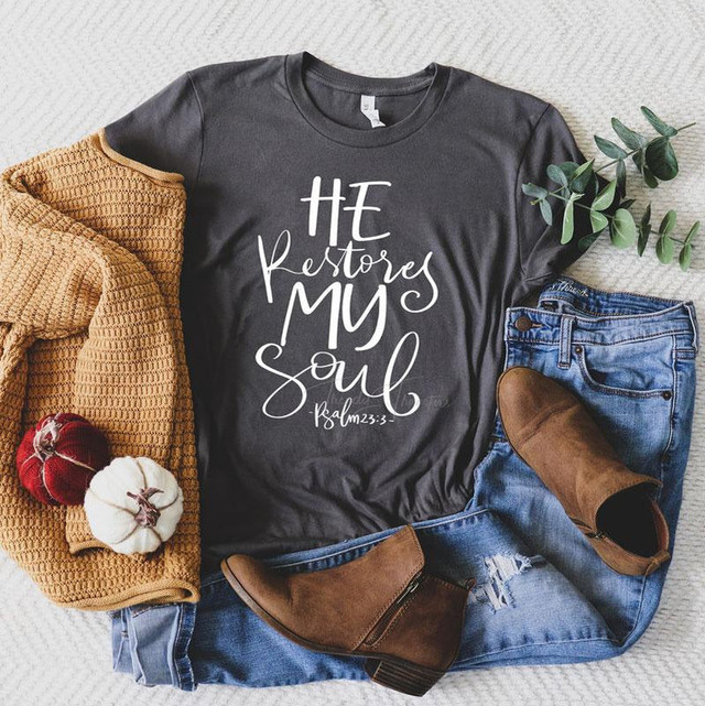 He Restores My Soul Screen Print Transfer, black T-shirt with white scripture text, paired with blue jeans, brown boots, a mustard-colored cardigan, and small decorative pumpkins, laid out on a light-colored surface.