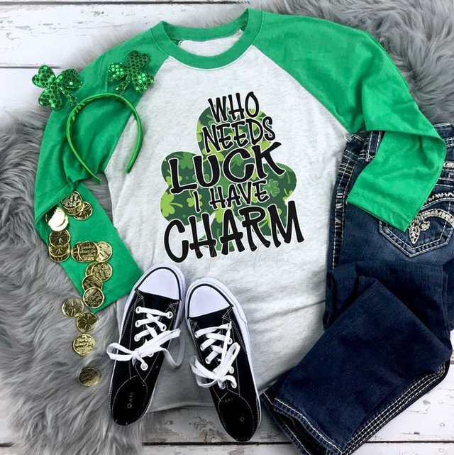 Who Needs Luck I Have Charm sublimation transfer t-shirt, green and white baseball tee with shamrock design and text, surrounded by St. Patrick's Day accessories like shamrock headbands, gold coins, and casual sneakers.